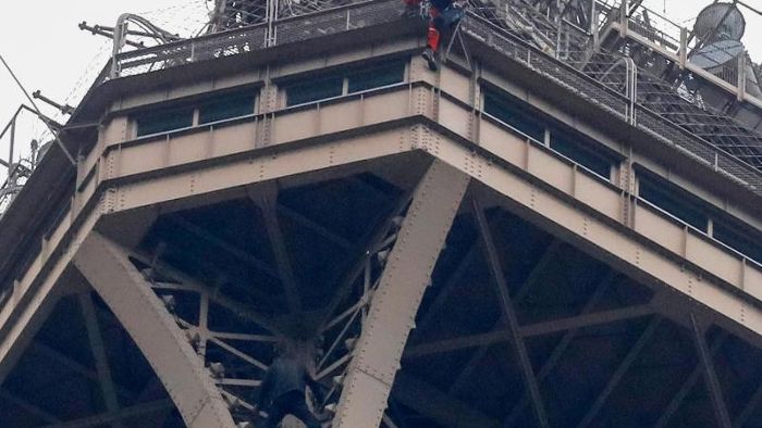 Mann klettert auf Eiffelturm und klammert sich fest